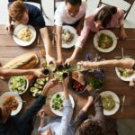 Top down view of a group of friends around a table at a brunch party cheersing their drinks