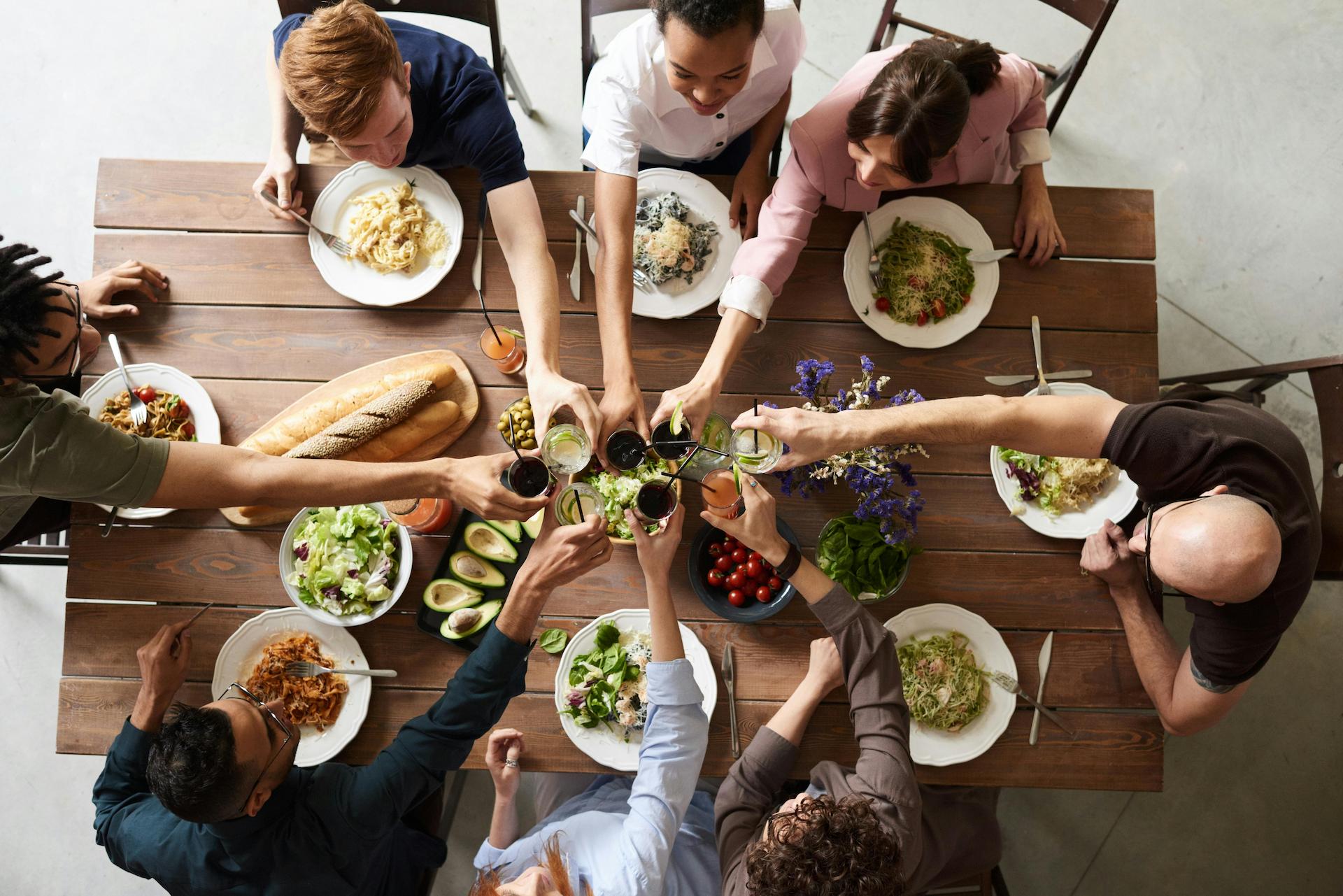 Top down view of a group of friends around a table at a brunch party cheersing their drinks