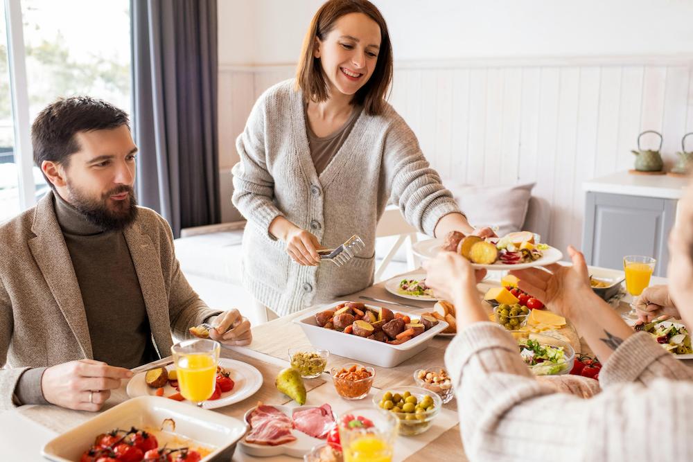 People at a table at a brunch party passing a dish across a table filled with food