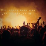 People in the crowd of a concert with event insurance, hands in the air looking toward an orange lit up stage