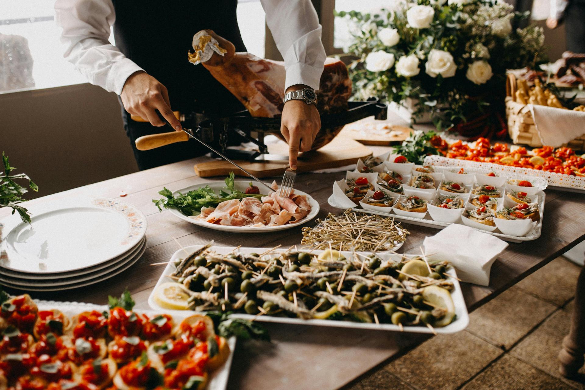 Food station at an event with various bit sized snacks to choose from and a chef carving a ham leg