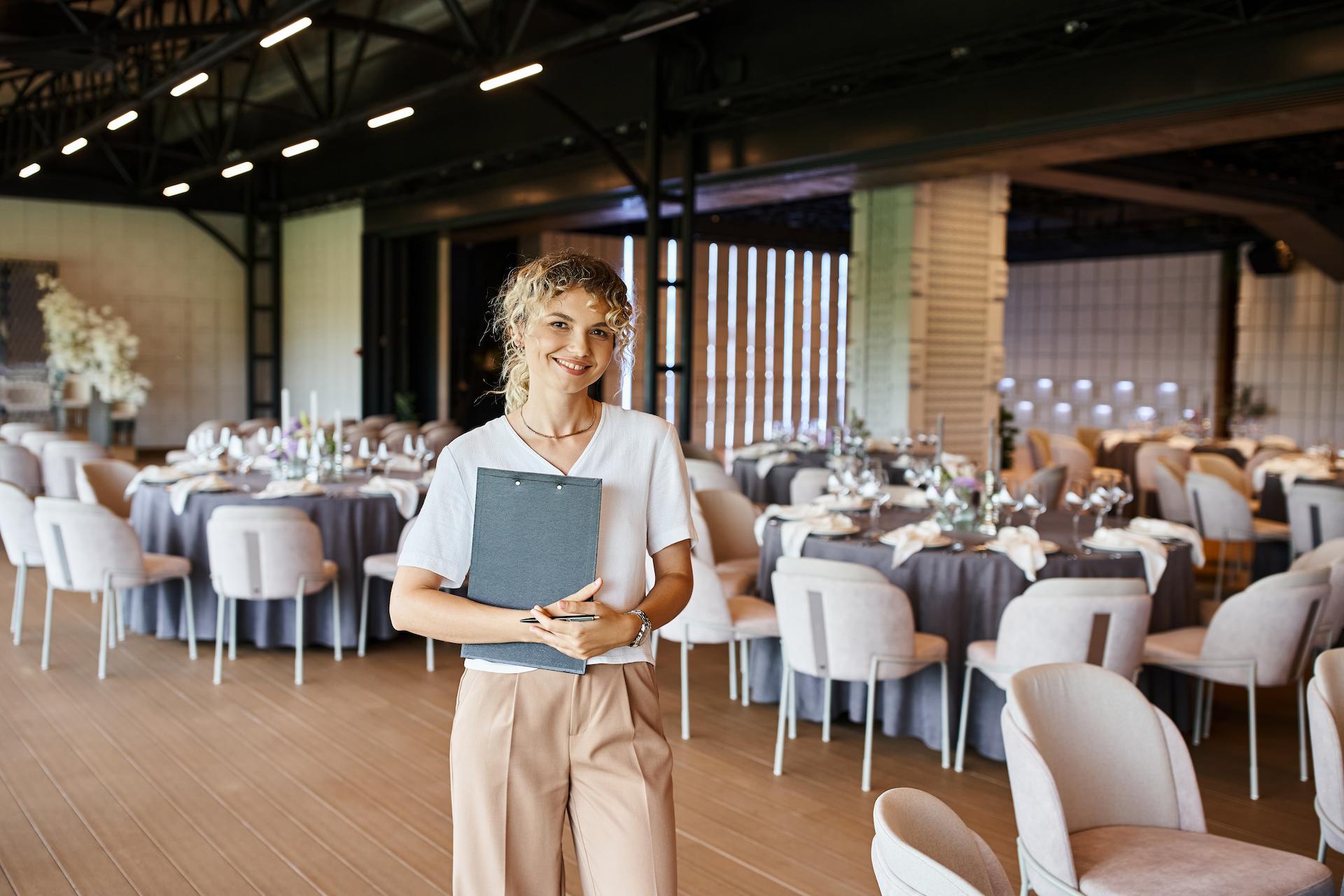 Event planner standing in a large venue room with a clipboard