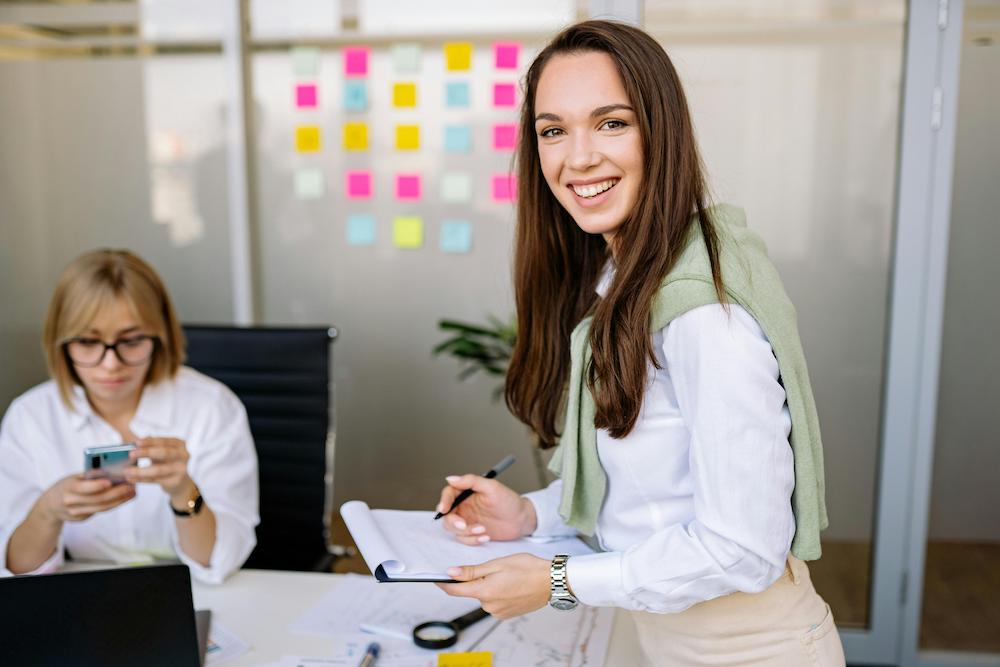 What is an event planner - young woman smiling at the camera while organising an event from an office space