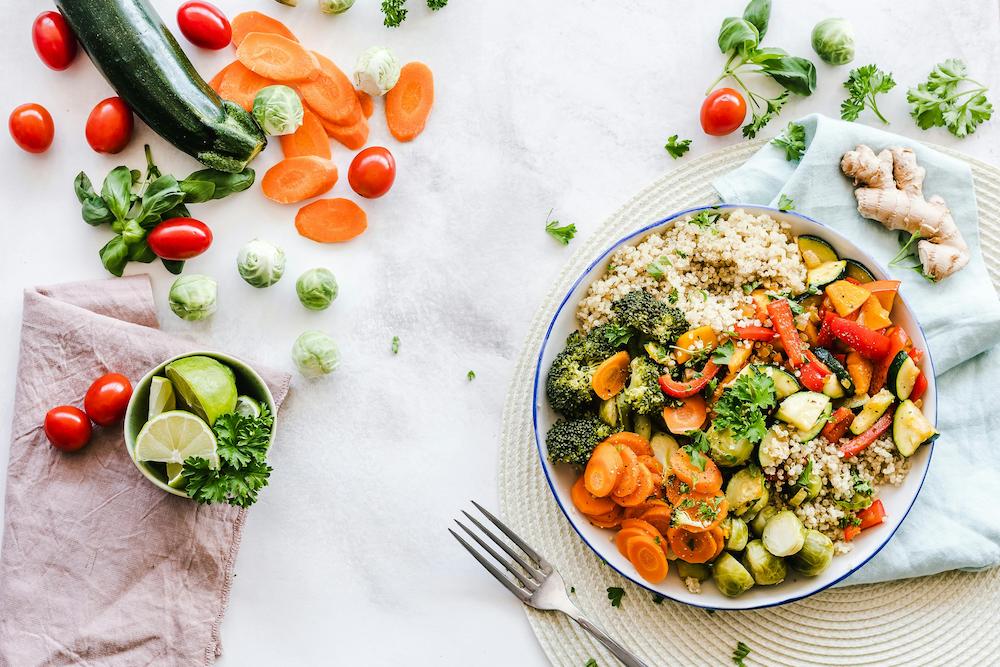 Top down view of a healthy meal in a bowl with some vegetables scattered around on the table