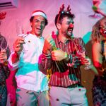 A group of work colleagues havin g a great time at a Christmas party ideas in Brisbane popping bottles of champagne and wearing reindeer antlers