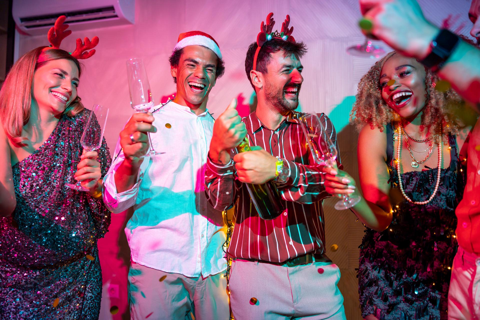 A group of work colleagues havin g a great time at a Christmas party ideas in Brisbane popping bottles of champagne and wearing reindeer antlers