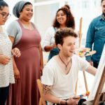 Live painting demonstration at an event with people crowded around the canvas, watching the artist work