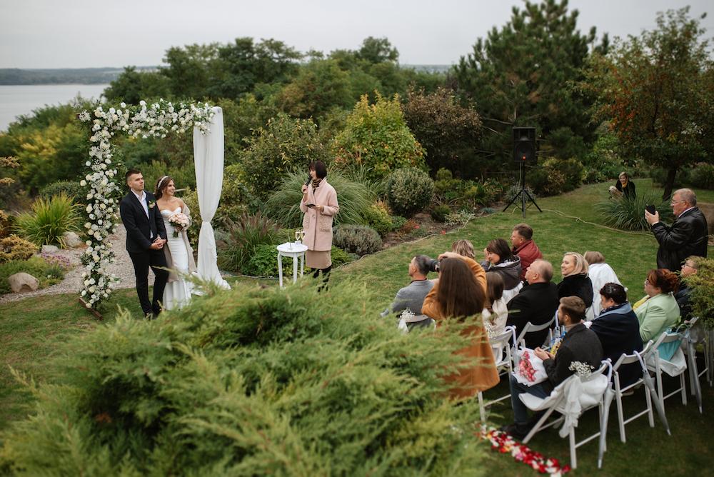 Beautiful lush garden setting for a wedding ceremony with a simple arbour and a small group of guests