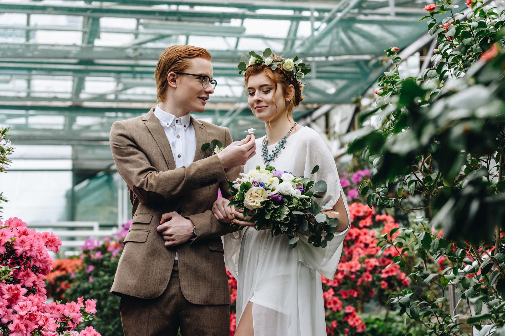 Young trendy bride and groom in a greenhouse setting with flowers surrounding them