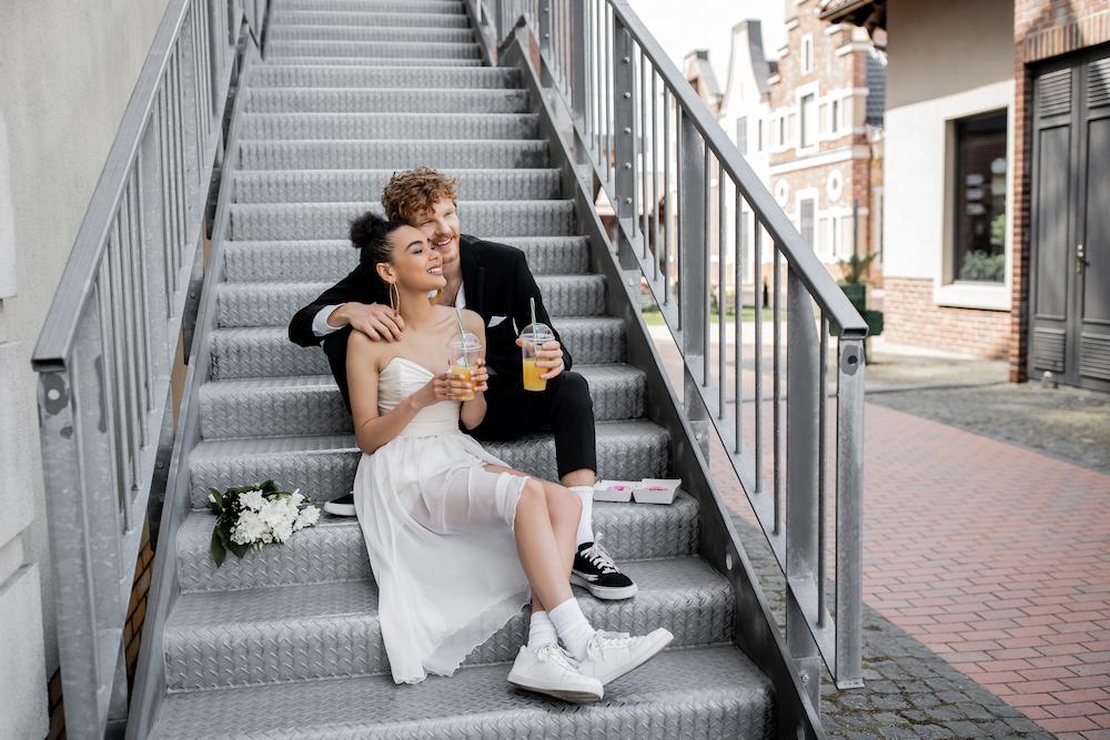 Young bride and groom sitting on stairs with drinks in hand after getting married at an urban wedding venue in perth