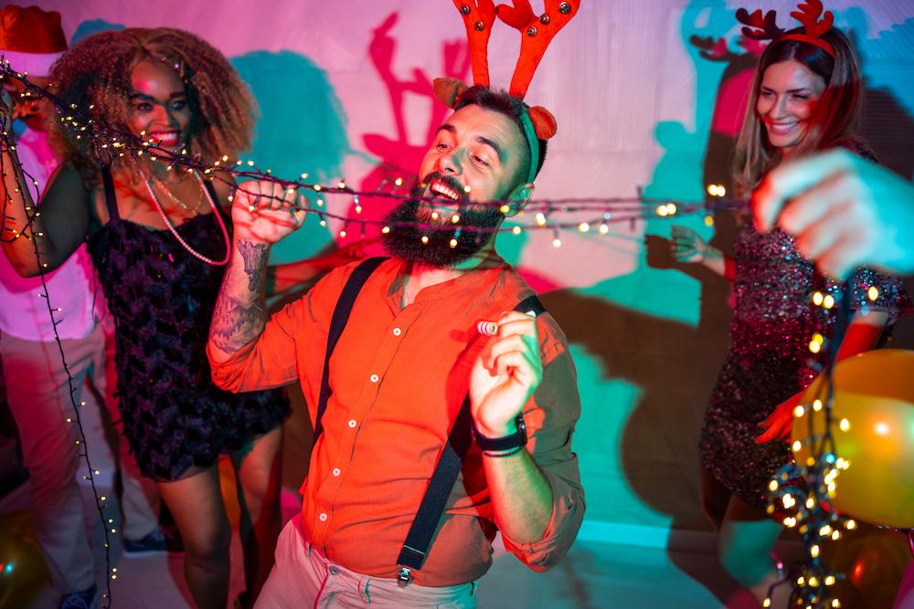 Colleagues at a Christmas party doing limbo with some fairy lights while wearing reindeer antlers