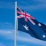 Australian Flag flying on a flag pole with a sunny blue sky behind