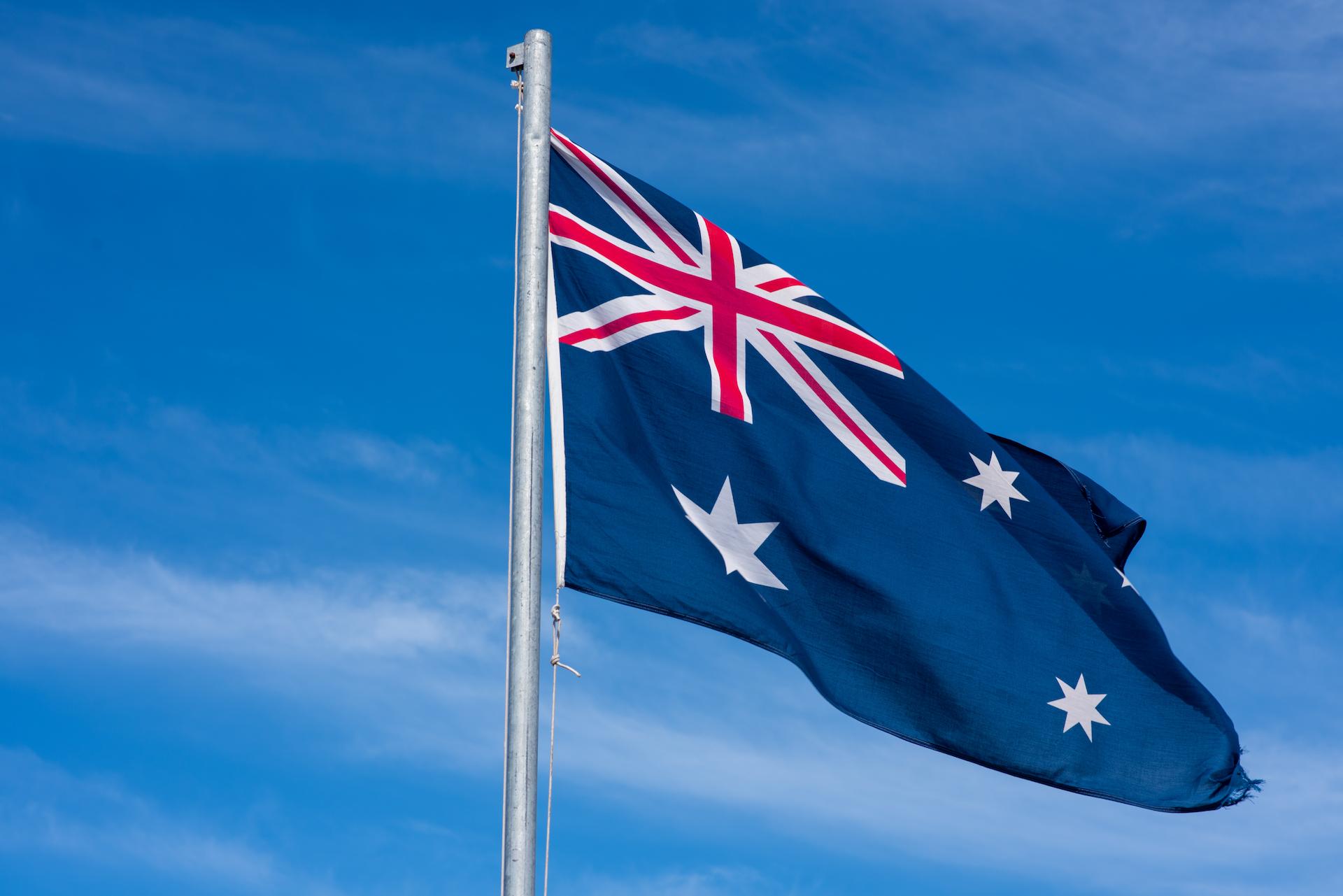 Australian Flag flying on a flag pole with a sunny blue sky behind