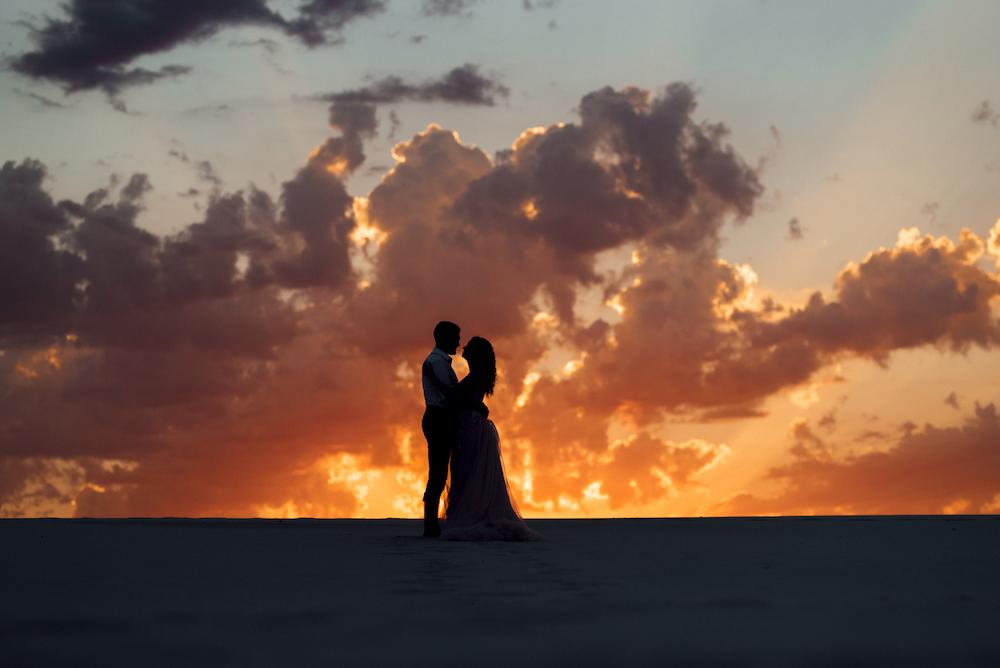 Beach wedding ideas include getting sunset photos such as this silhouette of a bride and groom with a vibrant, colourful sky behind them