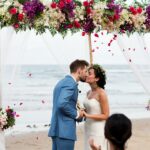 Bride and groom getting married on under an arbour on the beach is one of the beach wedding ideas for a beautiful day