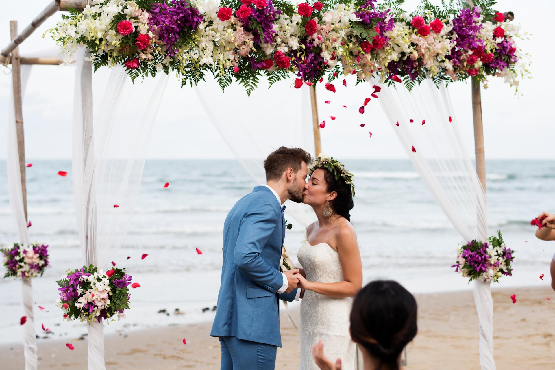 Bride and groom getting married on under an arbour on the beach is one of the beach wedding ideas for a beautiful day